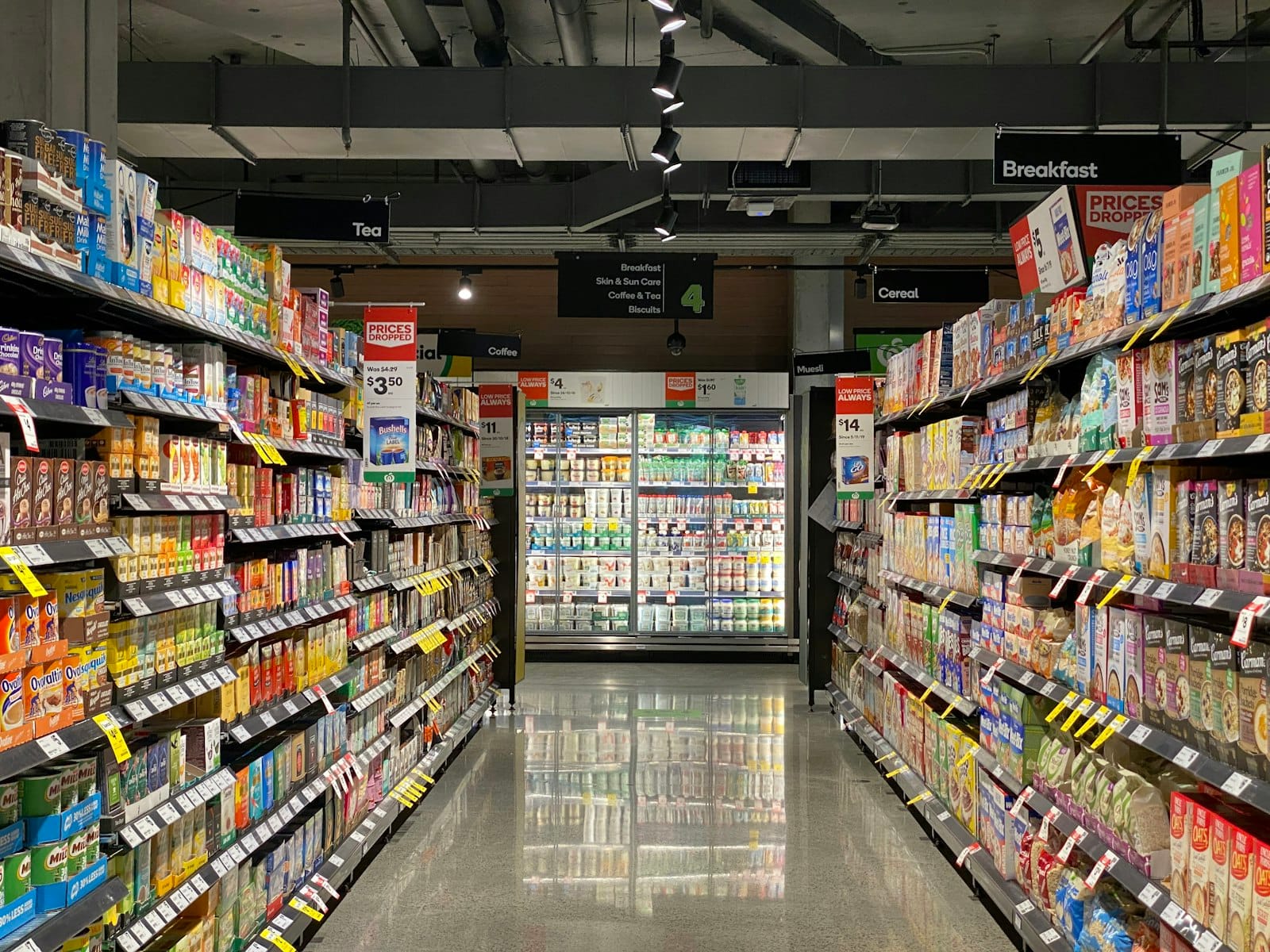 Grocery aisle with hanging category signs for breakfast, coffee, tea, and cereal
