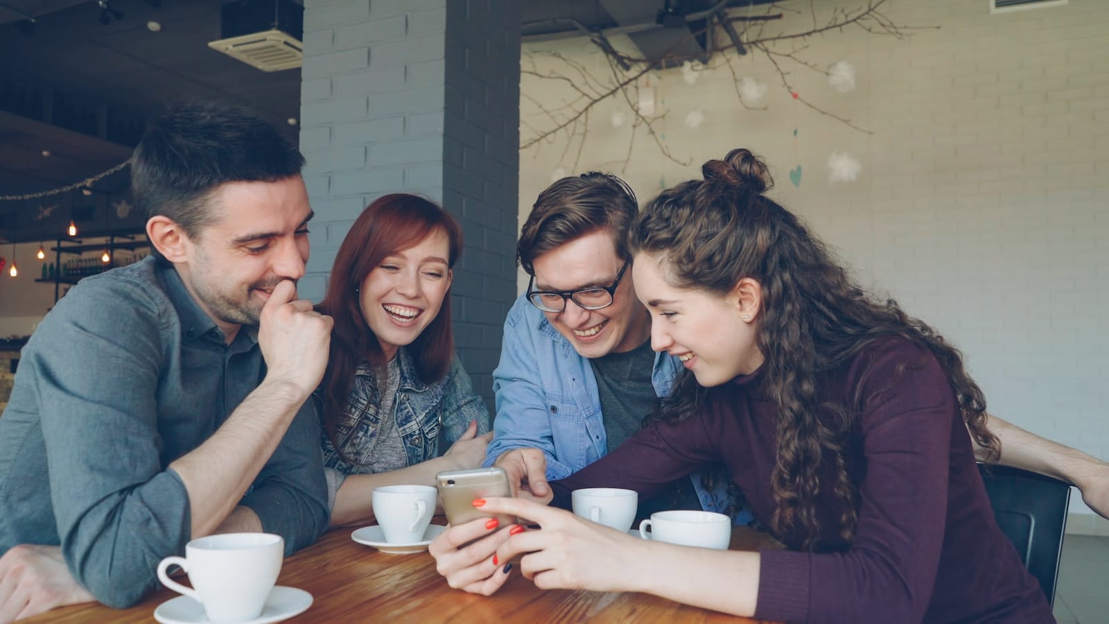 Friends gathered around one phone at a cafe table