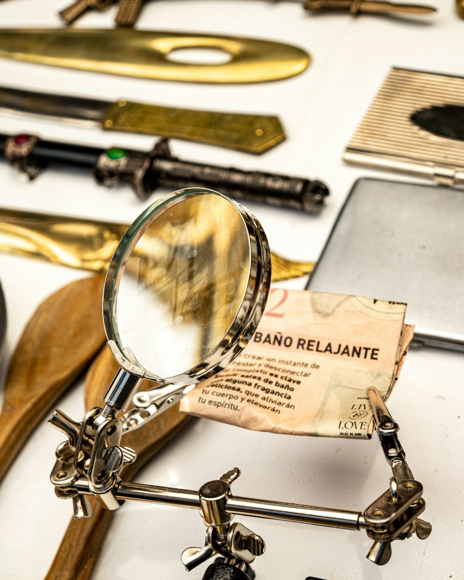A chrome magnifying glass on a stand examining a small paper, with other objects on a white table