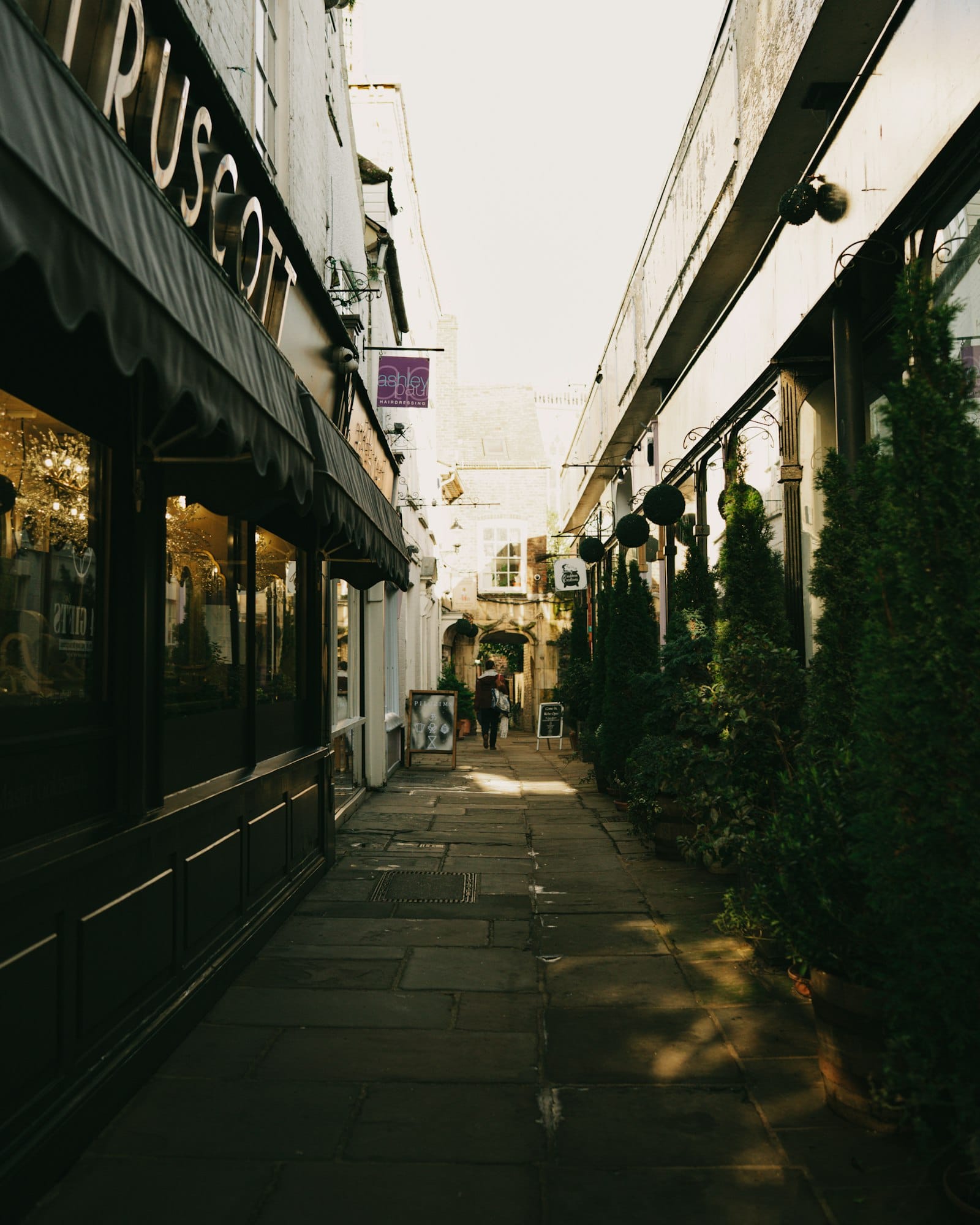 A narrow pedestrian alley of shop fronts leading toward a bright opening