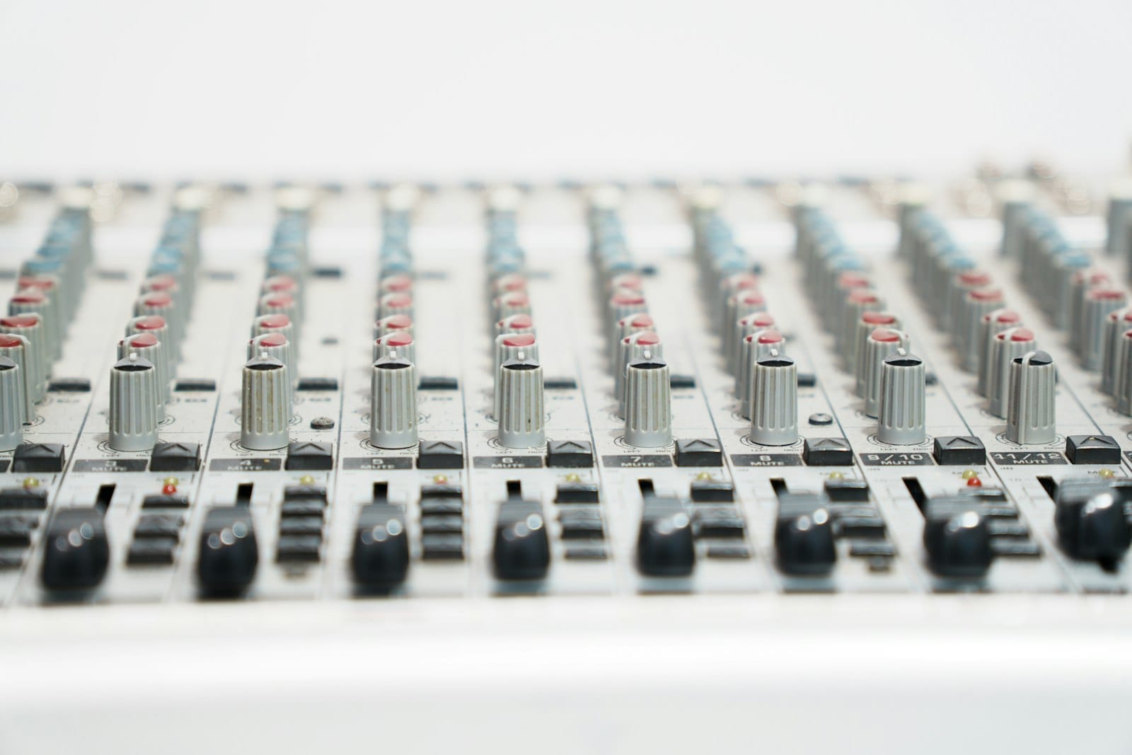 A close-up of an audio mixing board with sliders, knobs, MUTE buttons, and numbered channel strips