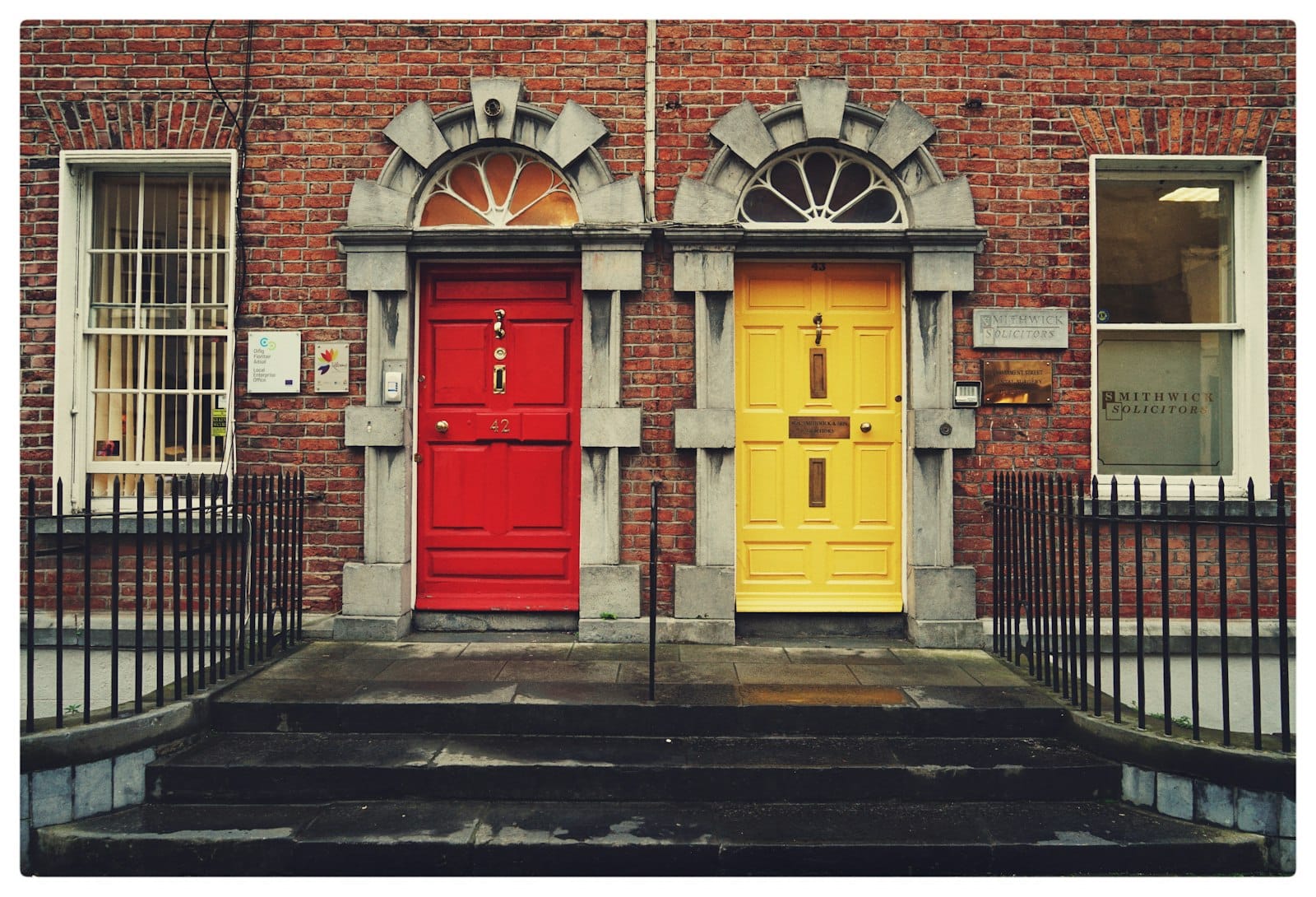 Two colored doors side by side on a brick building