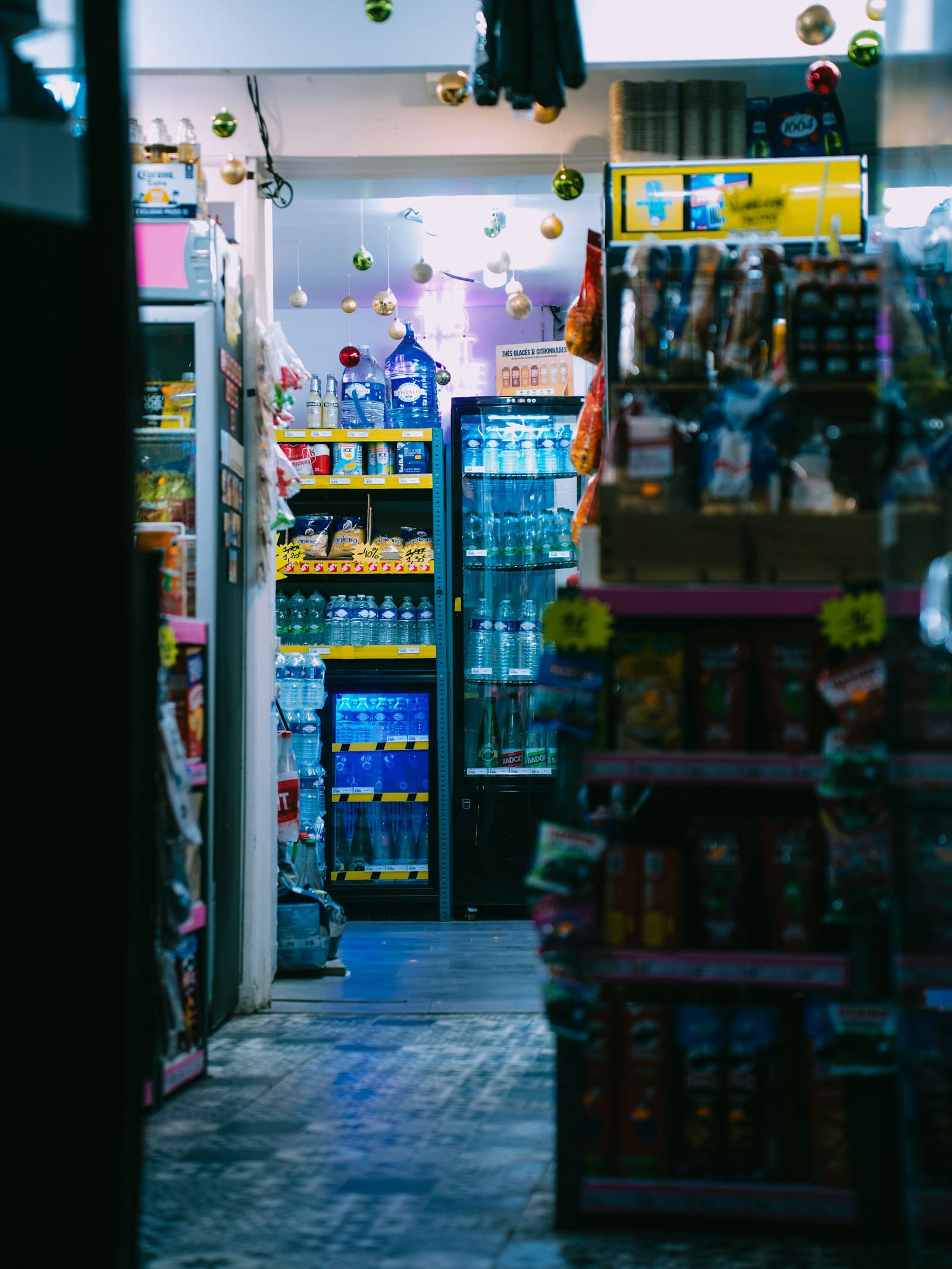 Bright convenience-store aisle with stocked shelves and a glowing cooler
