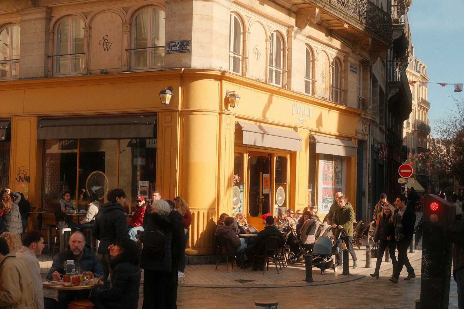 People sitting outside a yellow corner cafe on a sunny European street
