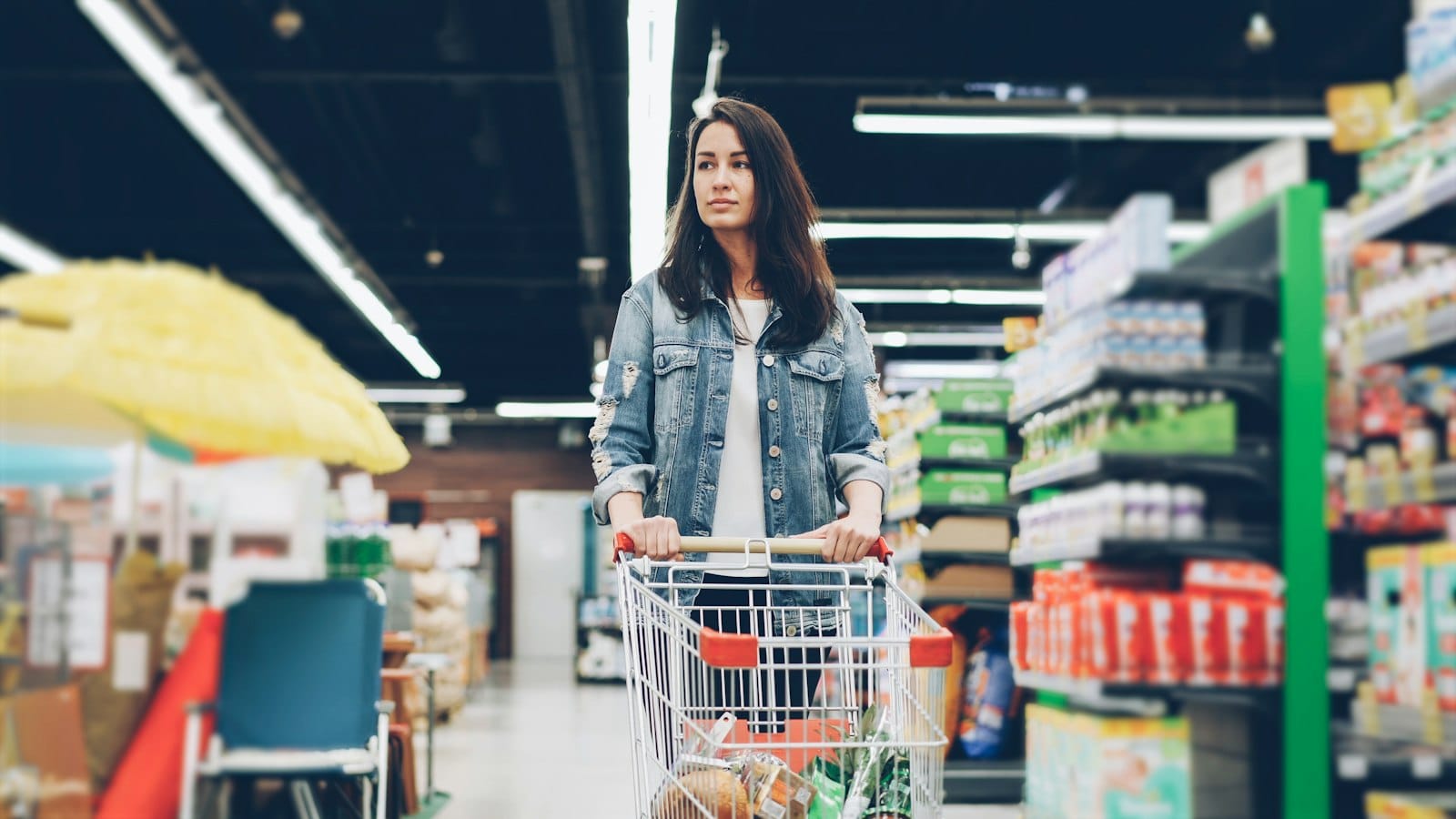 Woman browsing a supermarket aisle with a shopping cart