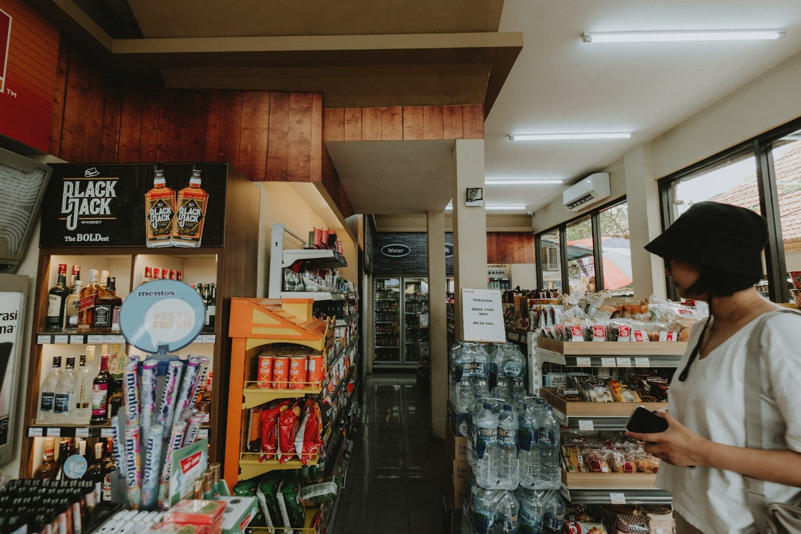 Woman browsing stocked shelves in a bright convenience-store aisle
