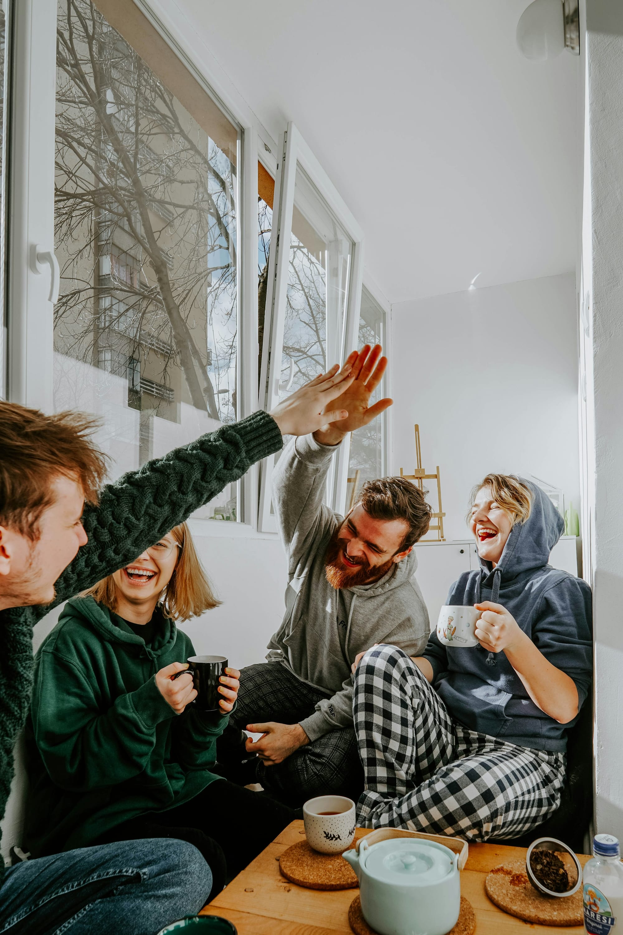 Four friends laughing and high-fiving over coffee