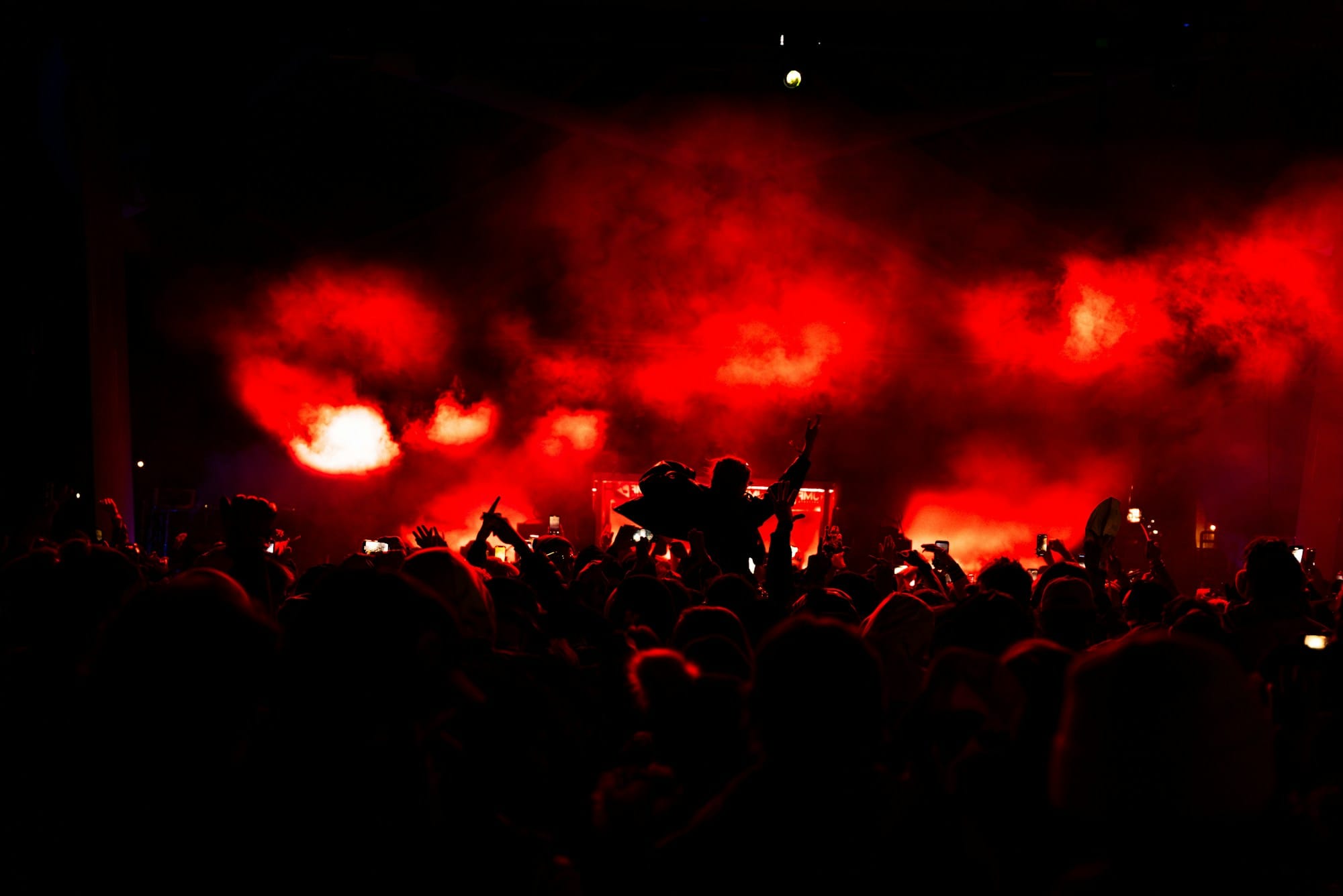 Concert crowd silhouettes under red stage lights and smoke