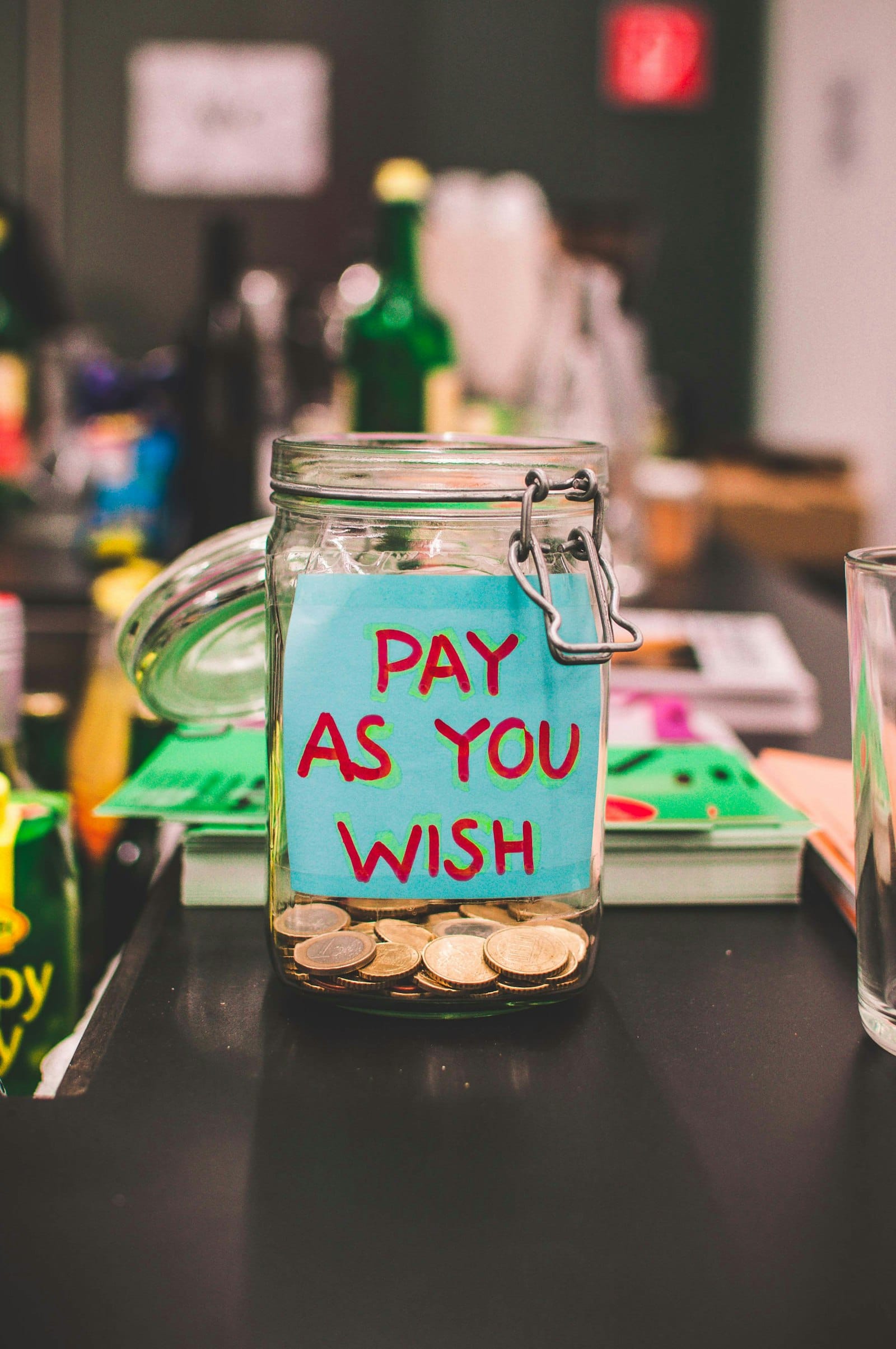 Clear glass tip jar with coins and a pay-as-you-wish label