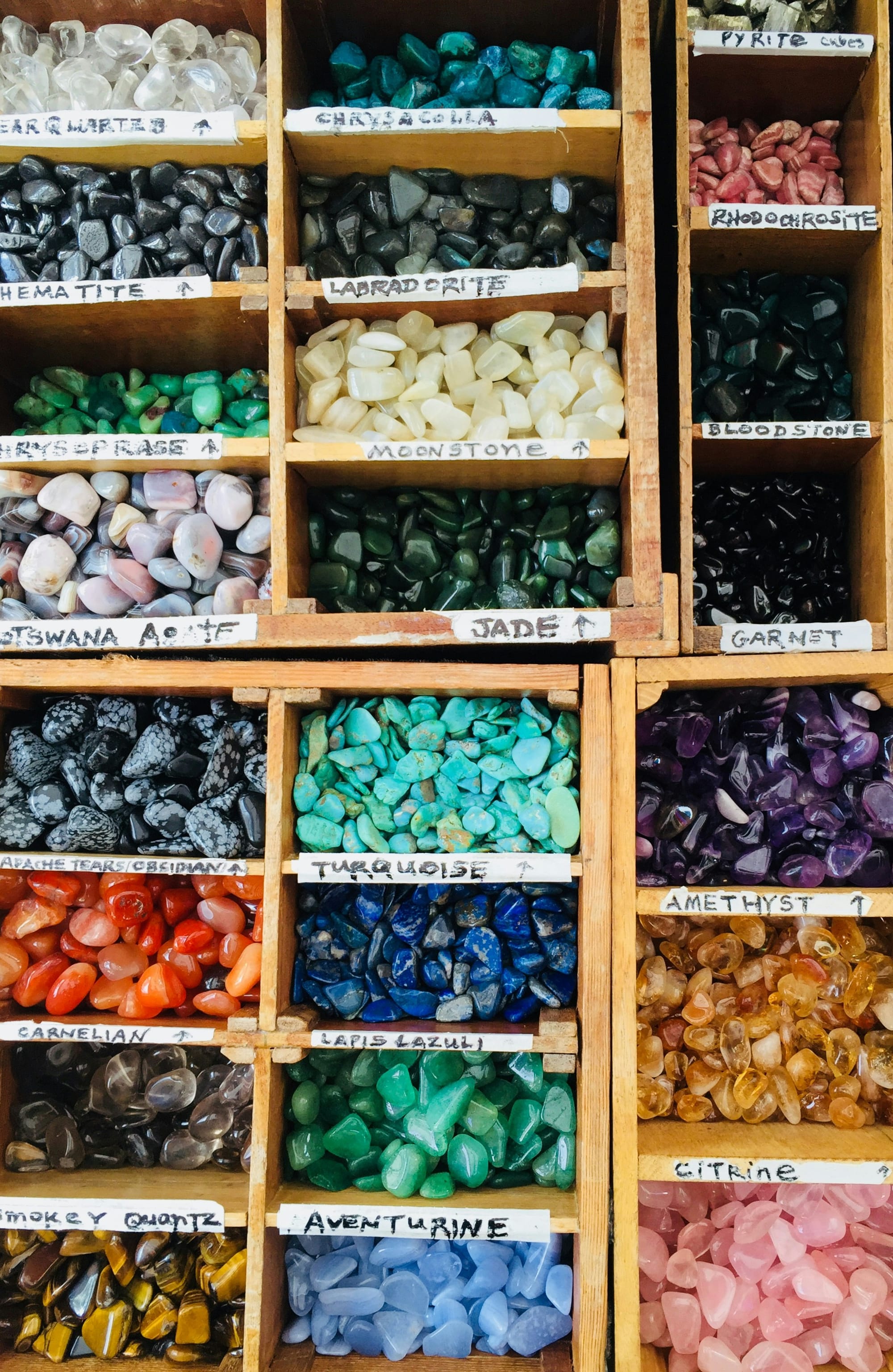 Assorted colorful gemstones in labeled wooden trays