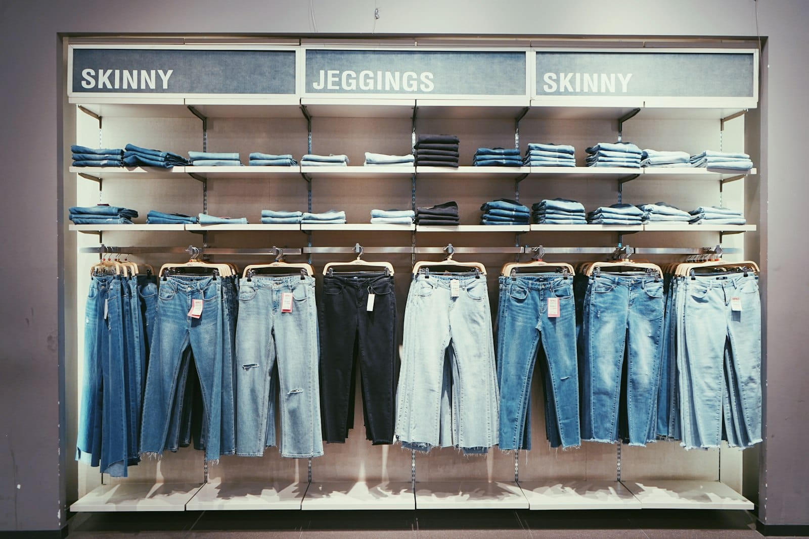 Denim styles on a retail rack with visible hang tags under clear section signs