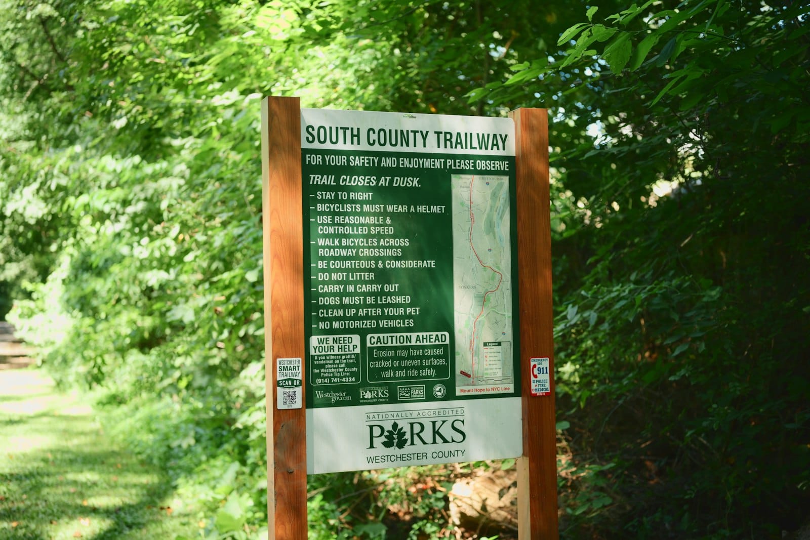 A green trailway sign posted on wooden posts listing trail rules beside a map