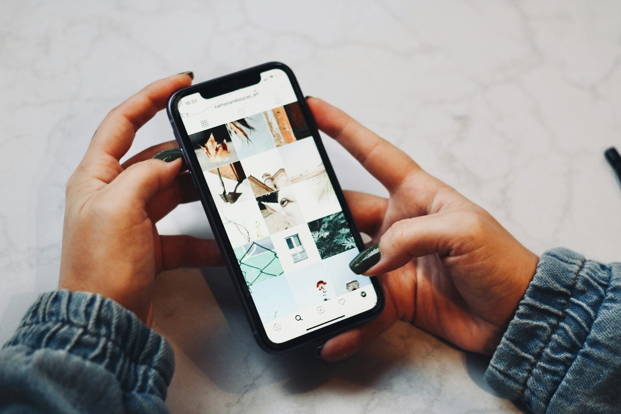Hands holding a phone that shows a photo-grid profile page
