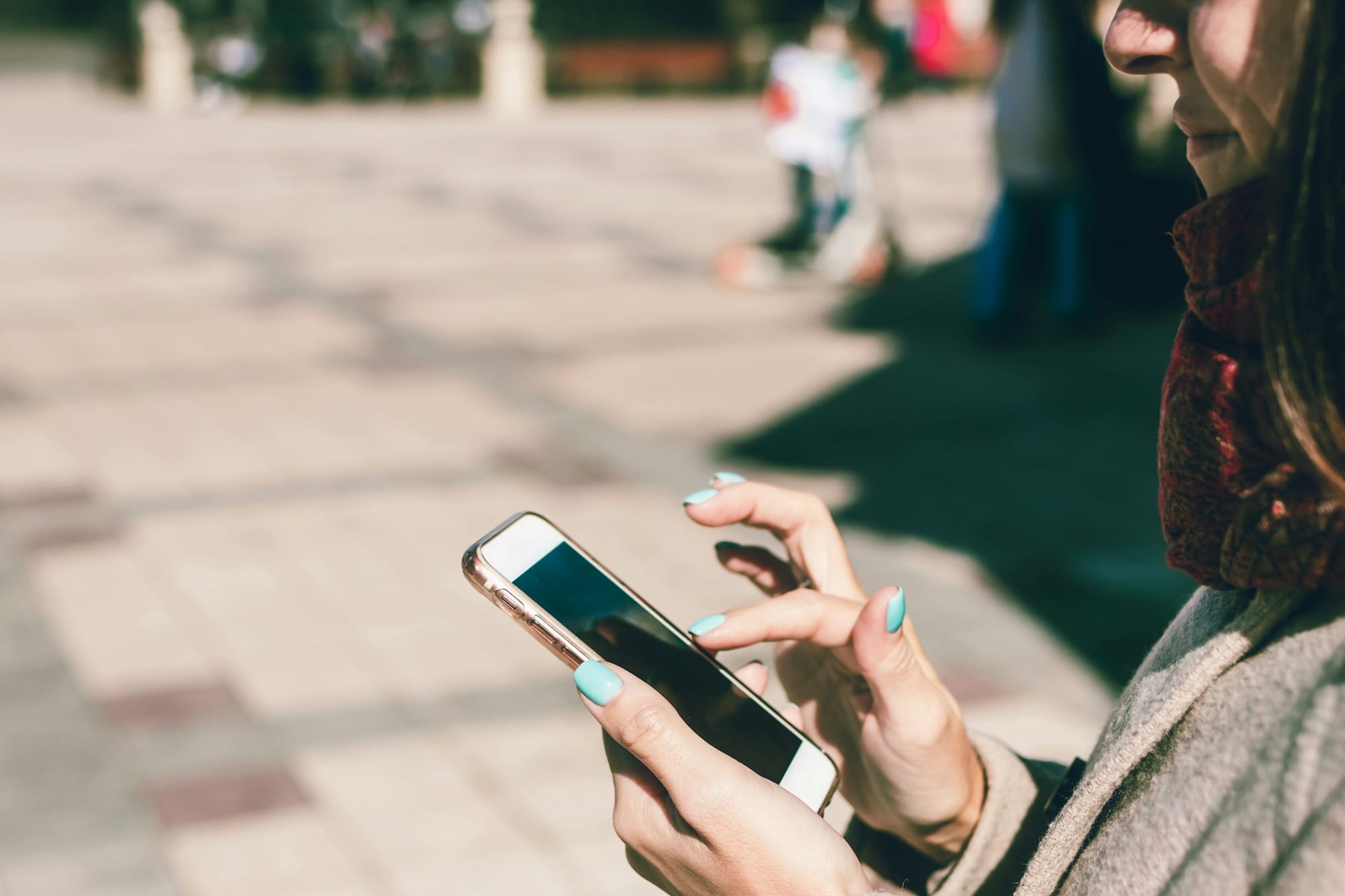 Person scrolling on a smartphone outdoors on a sunny day