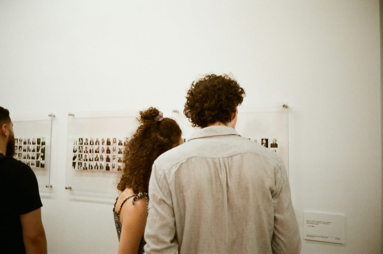 Two people from behind looking at grids of small portrait photos pinned to a white gallery wall