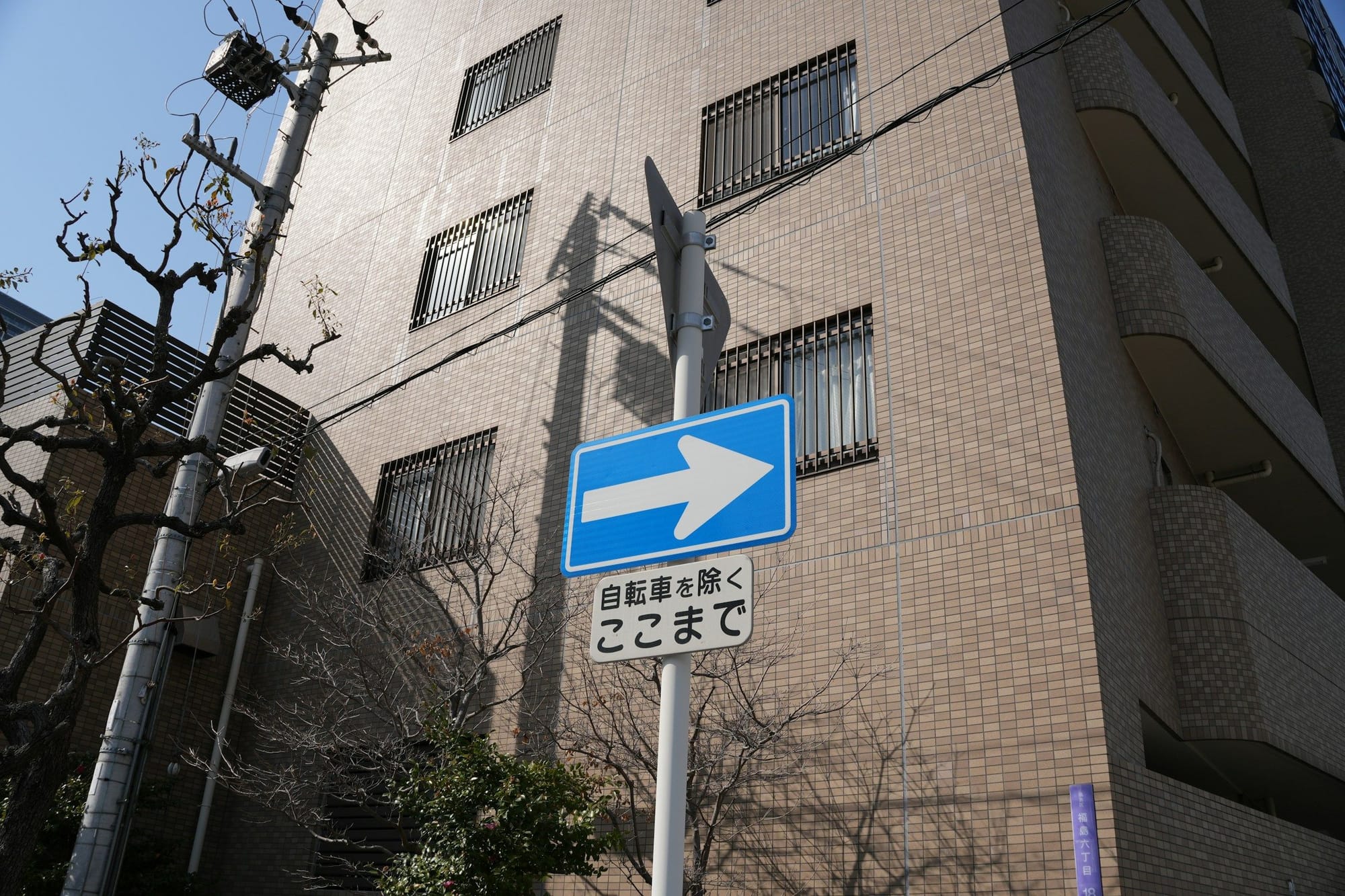Blue one-way street sign with a small Japanese text plate on a tiled building wall in Osaka