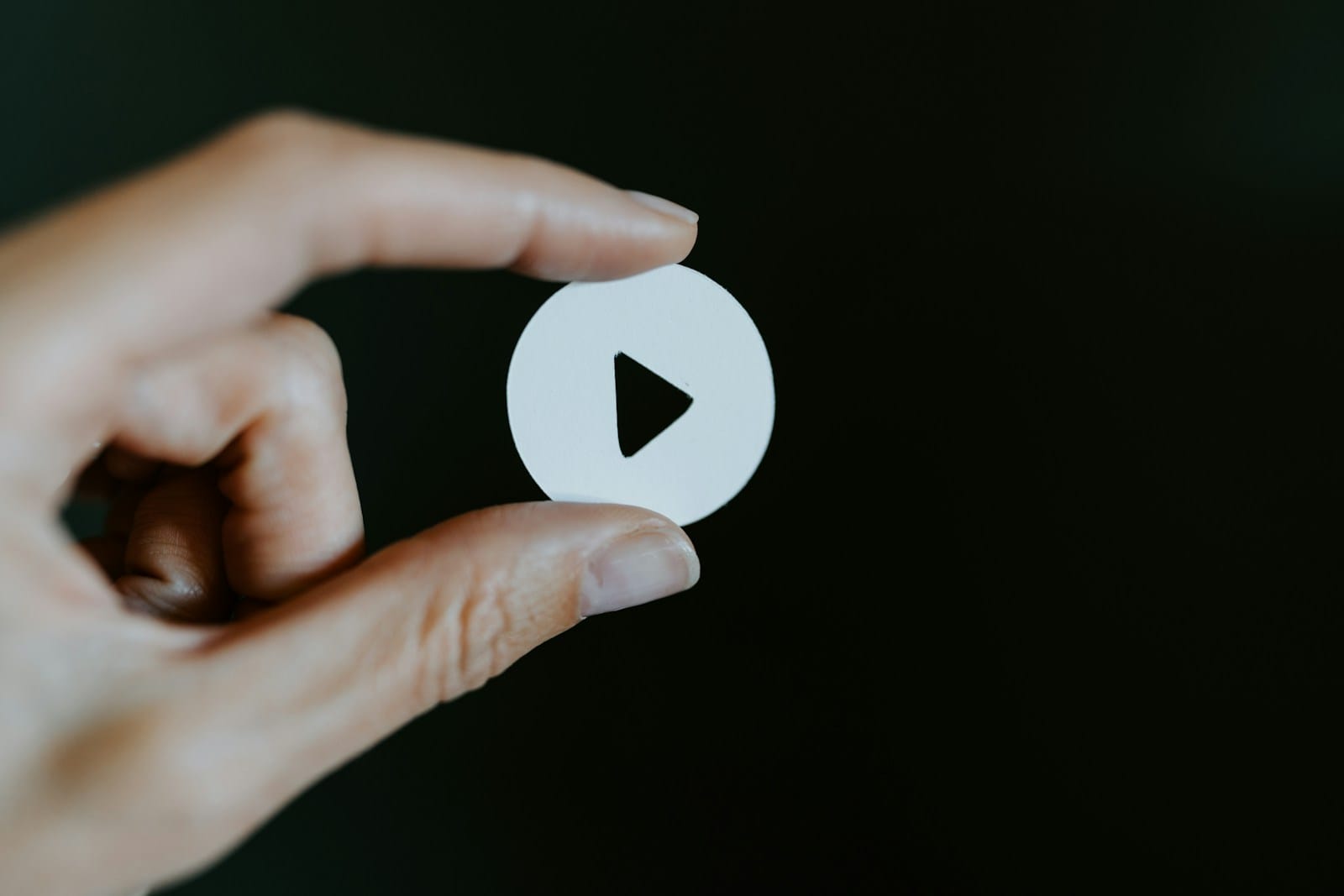 A hand holding a white paper cut-out of a video play button against a dark background