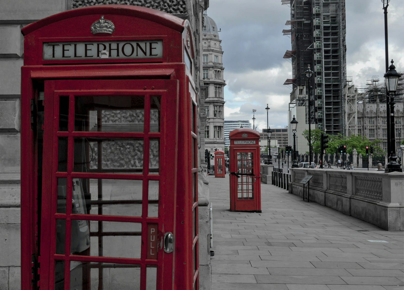 Three red British telephone boxes along an empty London pavement