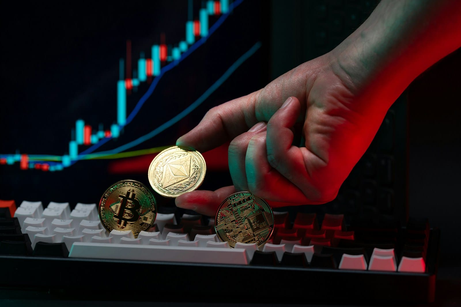 A hand placing a gold crypto coin on a keyboard in front of a price chart