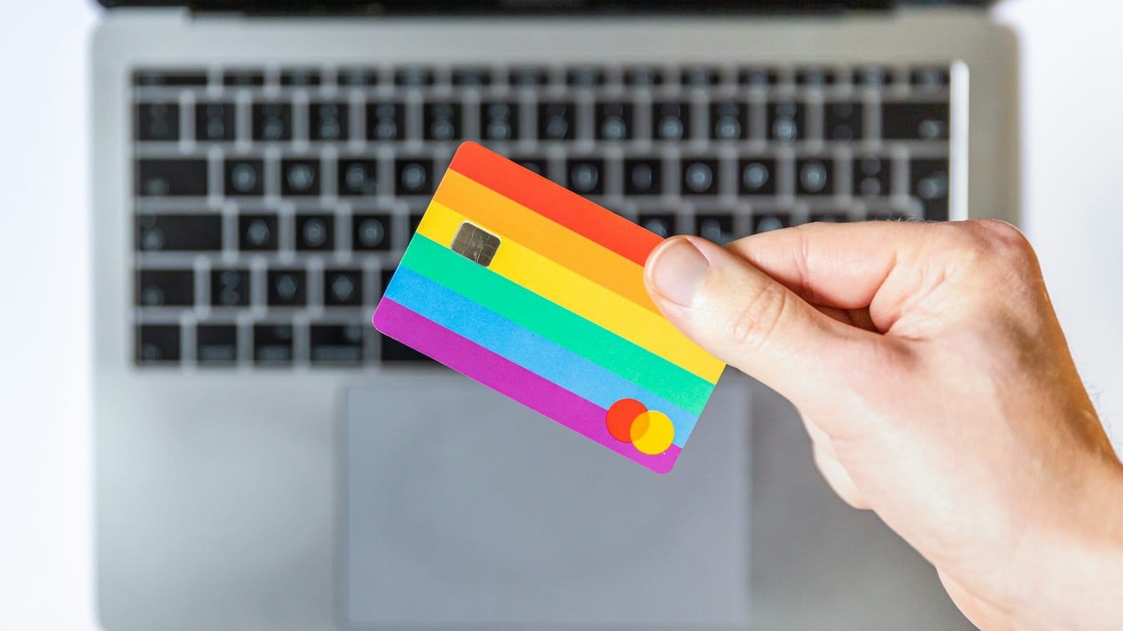 A hand holding a rainbow-striped payment card above a laptop keyboard
