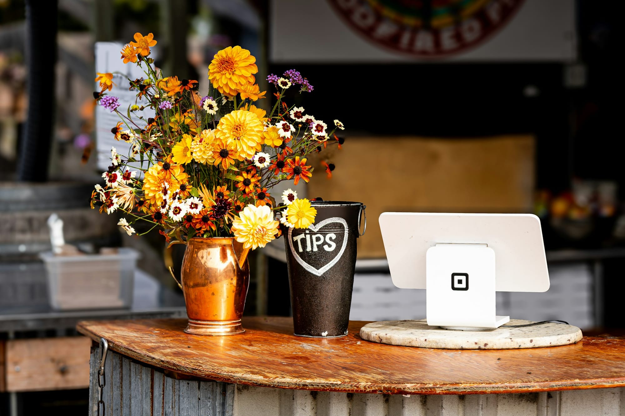 Checkout counter with flower vase, metal TIPS jar, and Square payment reader