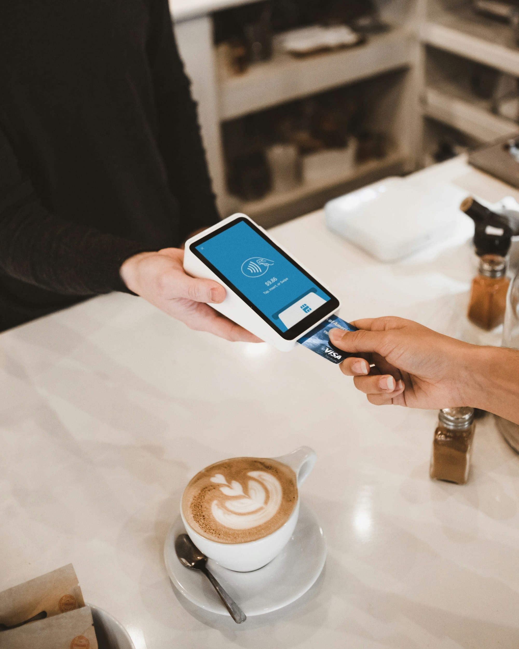Person inserting a credit card into a cafe payment terminal next to a latte