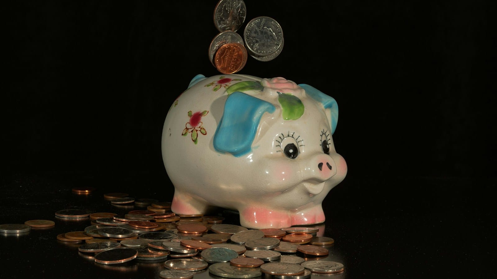Coins falling into a white ceramic piggy bank against a black background